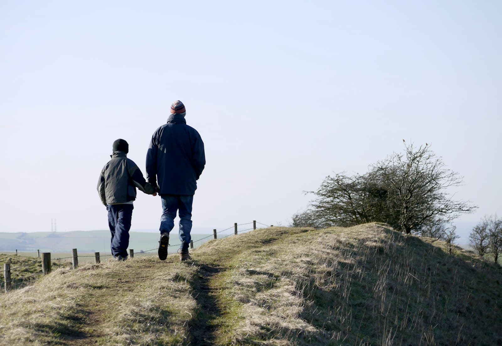 Een vader en zoon lopen hand in hand over een grasdijk
